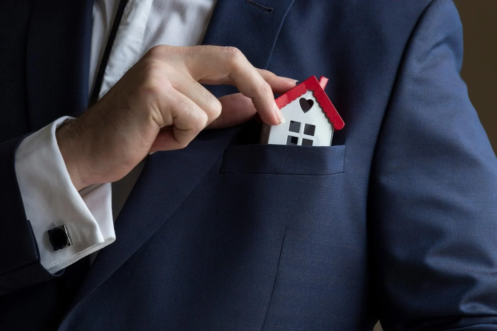 A person in a suit placing a miniature house model into their jacket pocket, illustrating a strategy for working with expired real estate listings