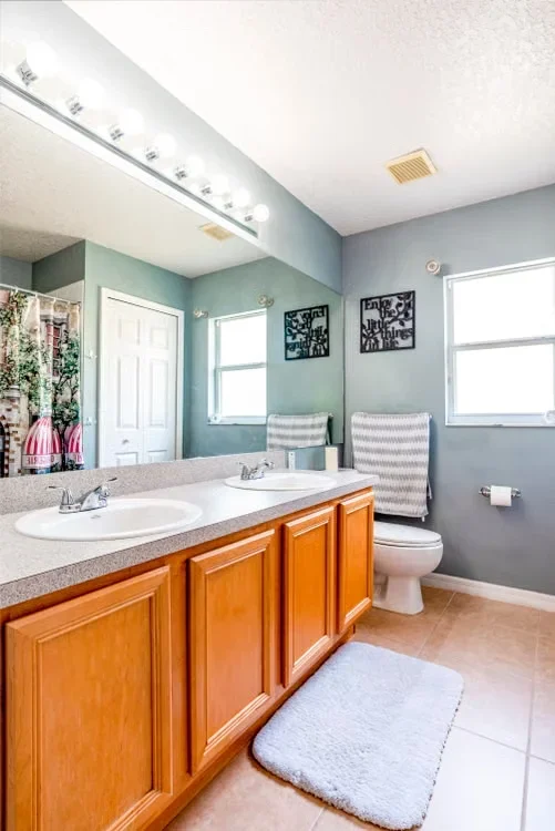 A blue painted bathroom with wooden cabinets, double sink, and toilet.