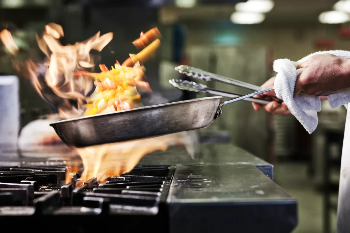 A hand holding a pan over fire, flipping some type of food.
