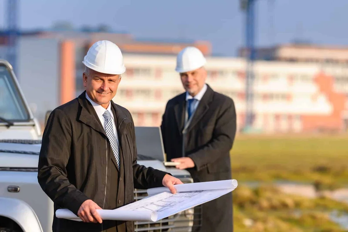 Two architects at construction site review plans.
