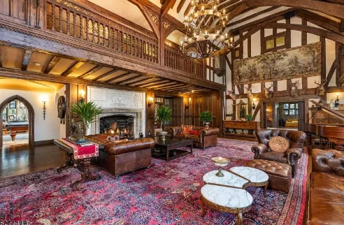 Medieval style living room with red carpet, three tiered chandelier, and multiple leather chairs and sofas.