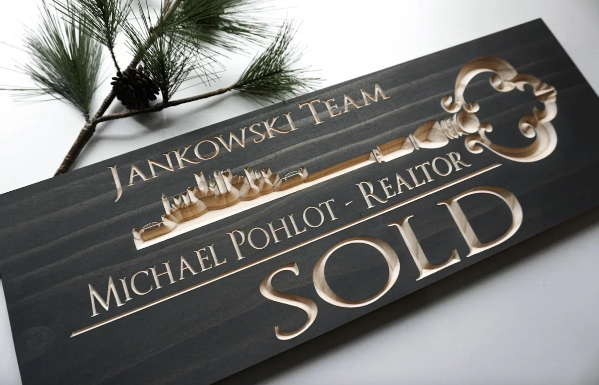 A dark wooden sign with carved white text that reads "SOLD"