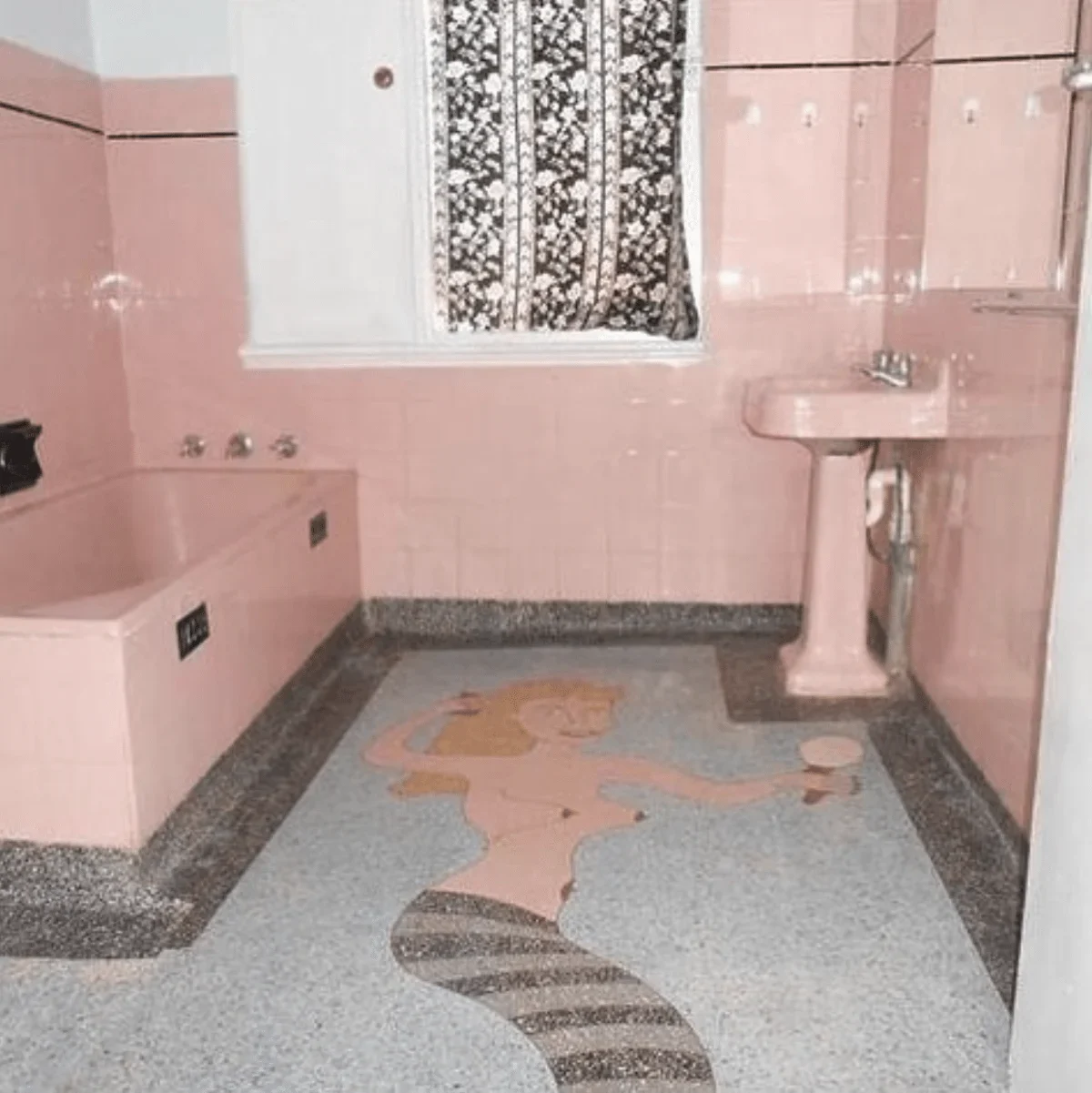 Tiled bathroom with pink tiles up the wall with matching pink sink and tub. The floor is a tiled mosaic of a mermaid holding a mirror and combing her hair.
