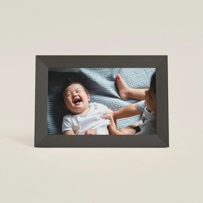 A digital photo frame with an image of two babies sitting on a bed on it.