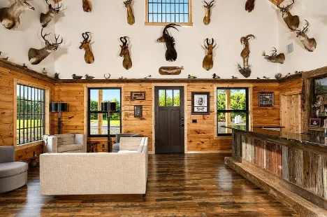 A cabin modern hunting cabin interior with a white couch to the left, and a bar area on the right. Hung on the walls are countless taxidermy mounts.