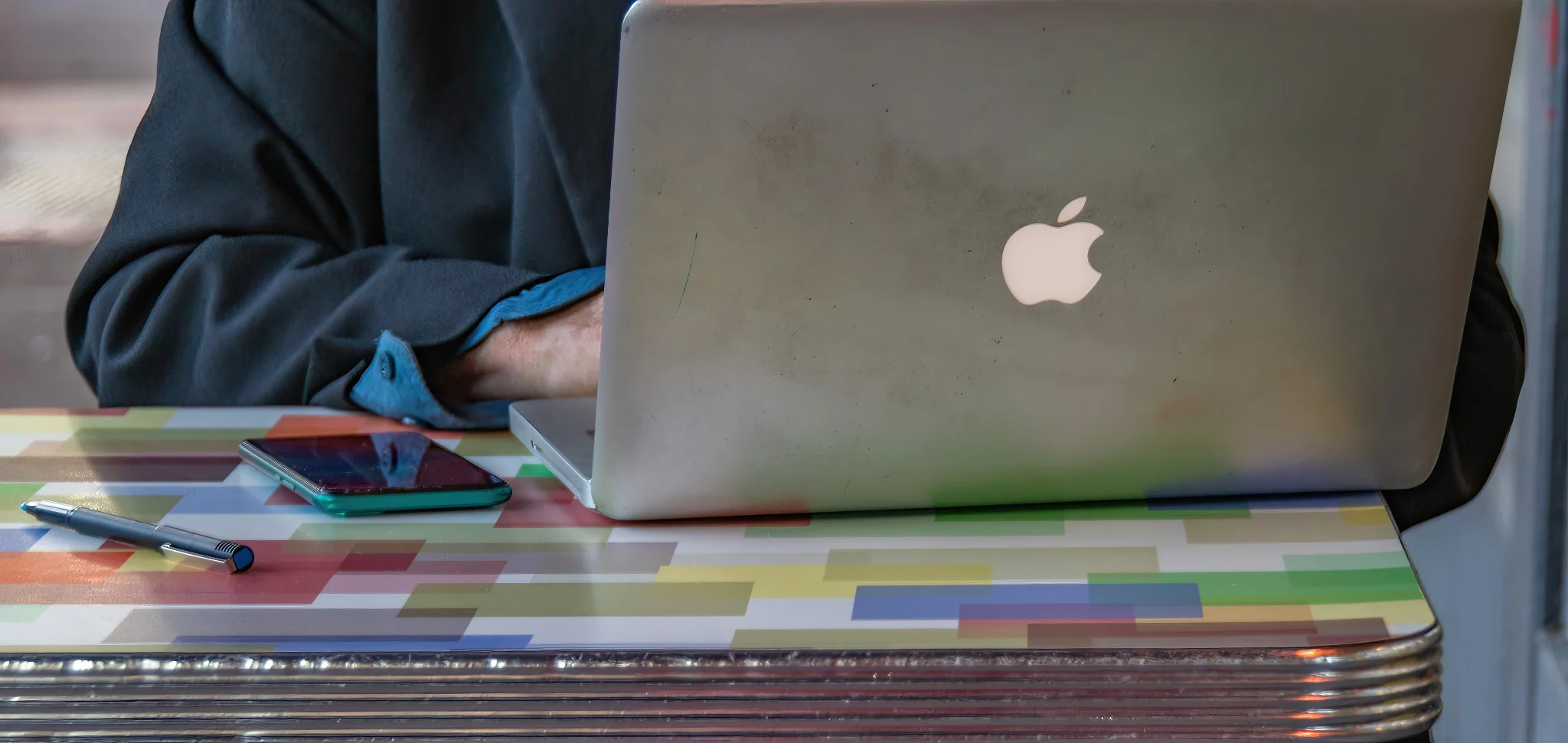 Mac laptop on colorful table with half of a person using it.